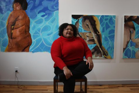LaNia Roberts, 25, poses for the camera in front of a variety of her self-portraits, Dec 1st. She does work in different mediums, though the works displayed are water and acrylic. Photo by Jackson Barnes.