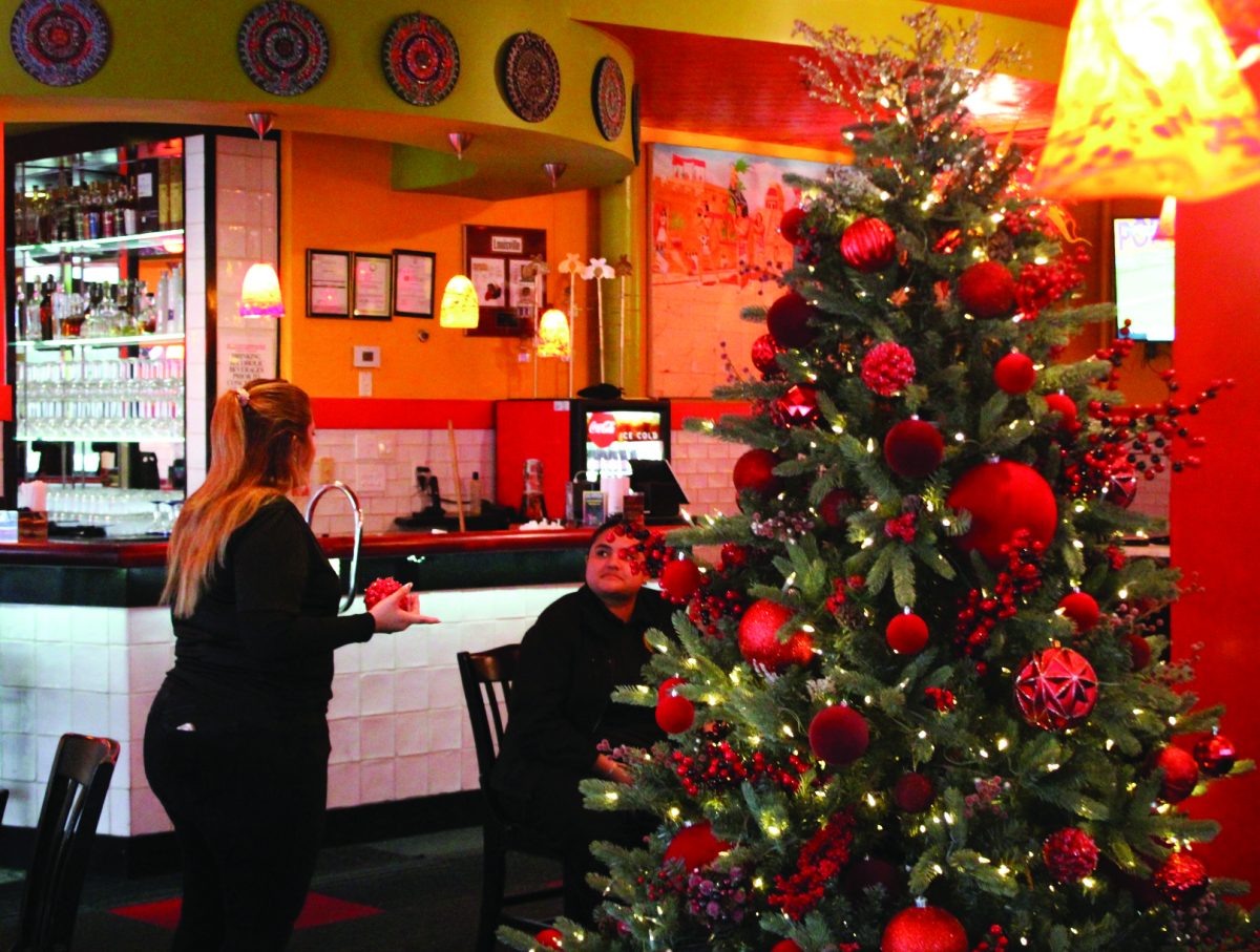 Seasonal Prep - Jocelyn Garcia, a waitress at Los Aztecas, places an 
ornament on the tree on Dec. 3 during her shift at the restaurant. The tree is the first Christmas decoration they have put up, complete with varying ornaments that match the restaurant’s decor.